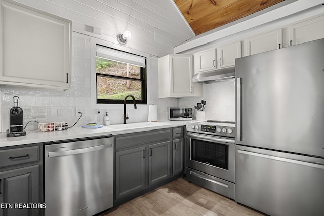 kitchen featuring stainless steel appliances, under cabinet range hood, gray cabinetry, a sink, and wooden ceiling
