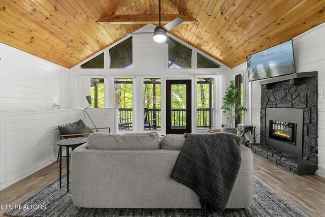 living area with wood ceiling, a ceiling fan, wood finished floors, a stone fireplace, and high vaulted ceiling