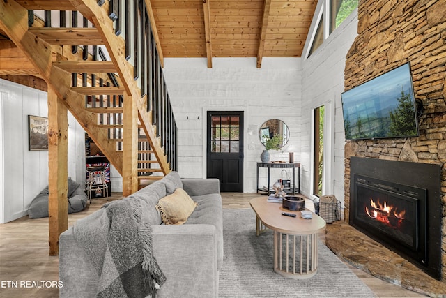 living room featuring high vaulted ceiling, wood ceiling, wood finished floors, a stone fireplace, and beamed ceiling