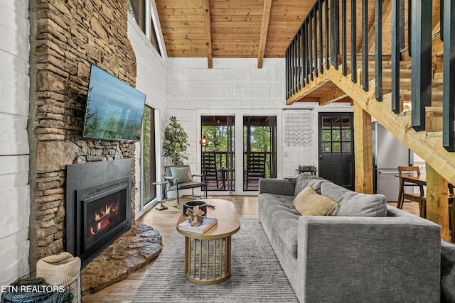 living area with wood finished floors, wood ceiling, high vaulted ceiling, beam ceiling, and a stone fireplace