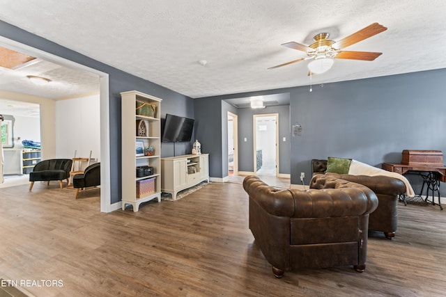 living area featuring a textured ceiling, wood finished floors, a ceiling fan, and baseboards