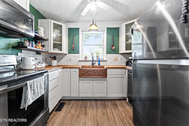 kitchen with appliances with stainless steel finishes, butcher block countertops, a sink, backsplash, and a textured ceiling