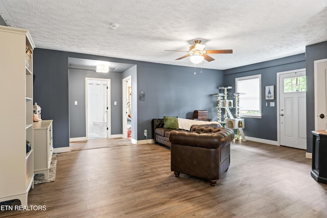 living room with a textured ceiling, a ceiling fan, wood finished floors, and baseboards