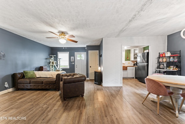 living room featuring light wood finished floors, a ceiling fan, baseboards, and a textured ceiling