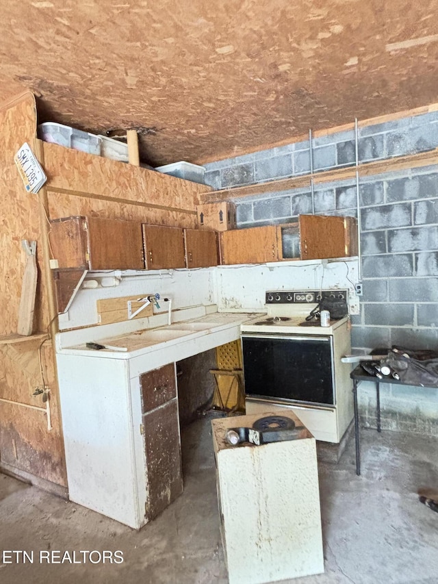 kitchen with unfinished concrete floors, white electric range, concrete block wall, a sink, and brown cabinetry