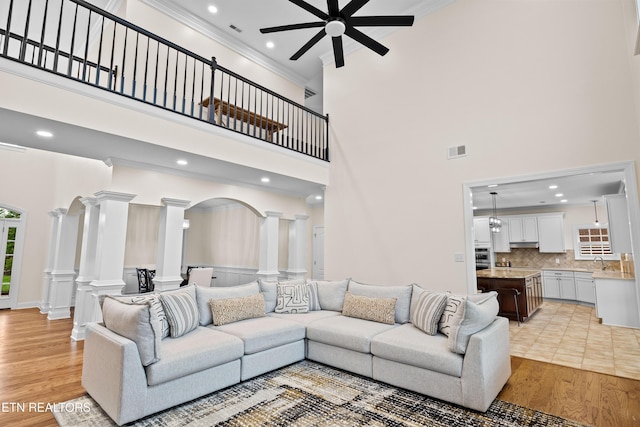 12618 Hunters Creek Ln, Knoxville, TN 37922 - living room featuring decorative columns, a ceiling fan, a towering ceiling, ornamental molding, and light wood finished floors