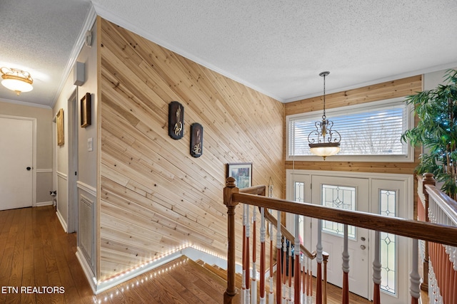hallway with a textured ceiling, ornamental molding, an upstairs landing, hardwood / wood-style floors, and wooden walls