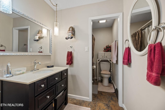full bath with baseboards, toilet, vanity, and stone finish floors