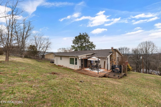 back of property featuring a wooden deck, a chimney, and a lawn