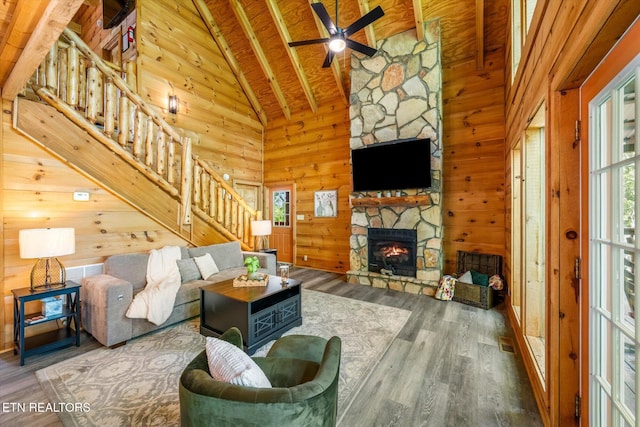 living room featuring a fireplace, stairs, wood walls, high vaulted ceiling, and a ceiling fan