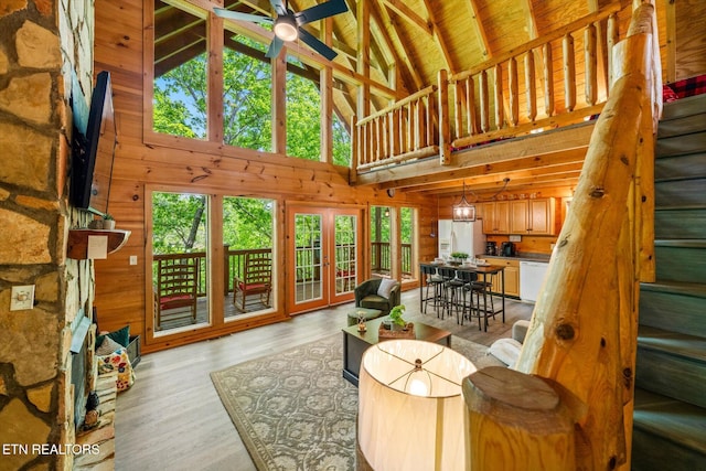 living area featuring high vaulted ceiling, wooden walls, a ceiling fan, beam ceiling, and light wood finished floors