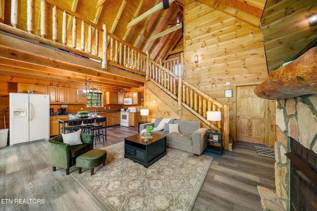 living room with high vaulted ceiling, stairway, wood walls, wood finished floors, and a stone fireplace
