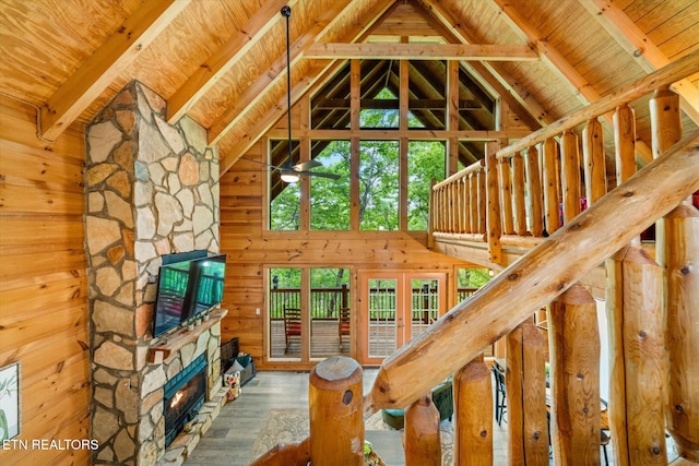 unfurnished living room with a stone fireplace, wood finished floors, wooden ceiling, and wood walls