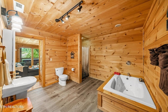 bathroom with a whirlpool tub, toilet, wood finished floors, track lighting, and wood walls