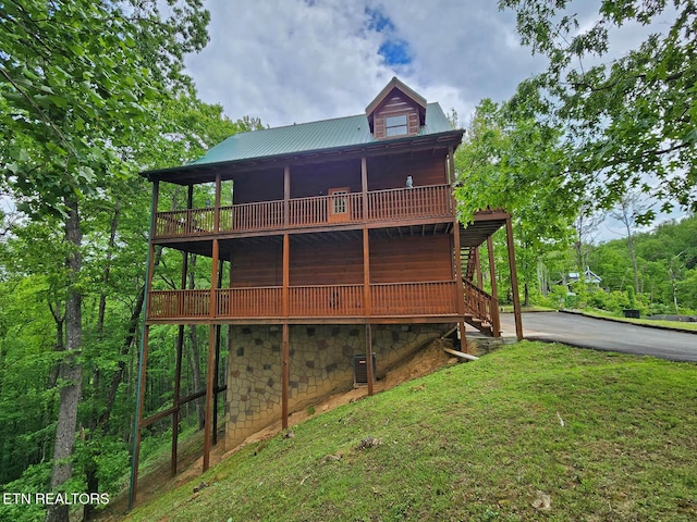 rear view of property with a wooden deck, a lawn, metal roof, asphalt driveway, and stone siding