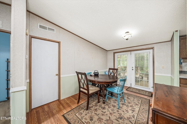 dining room featuring lofted ceiling, crown molding, wood finished floors, and a textured ceiling