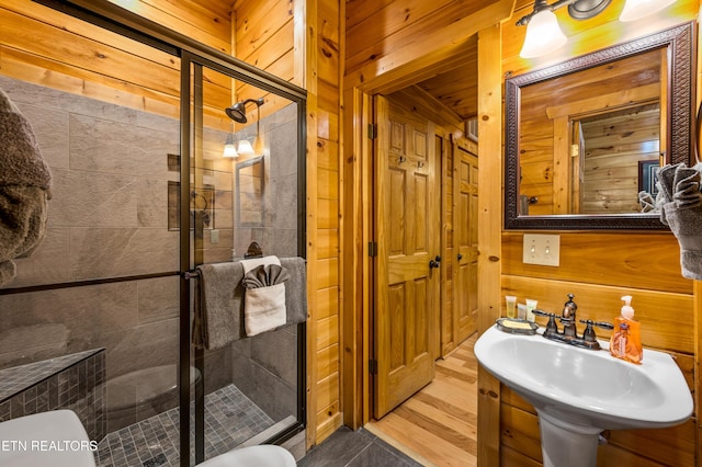 bathroom with wooden walls, a stall shower, toilet, and a sink