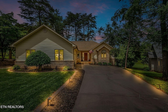 view of front facade featuring driveway, a lawn, and brick siding