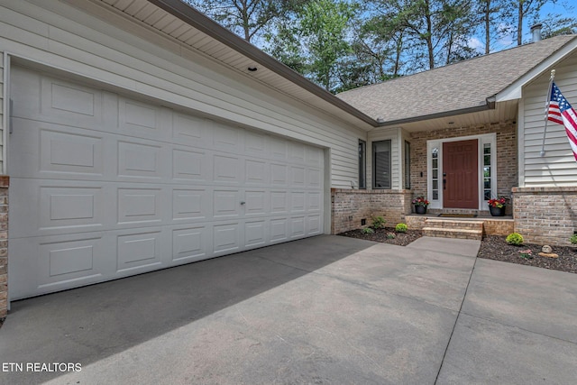 entrance to property featuring a shingled roof, brick siding, concrete driveway, and an attached garage