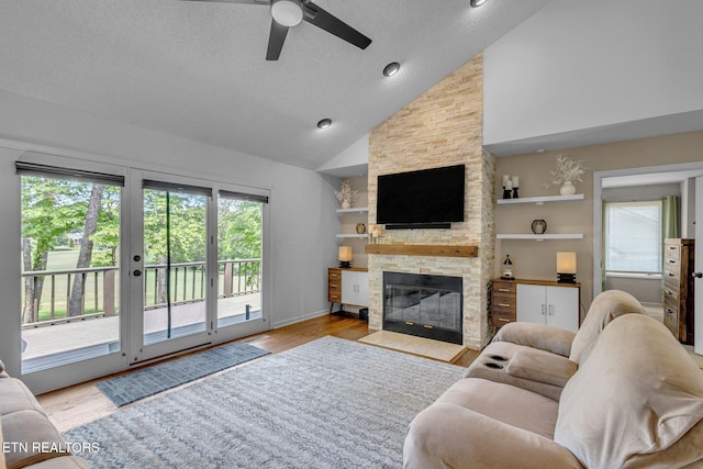 living room with ceiling fan, a stone fireplace, a textured ceiling, wood finished floors, and high vaulted ceiling