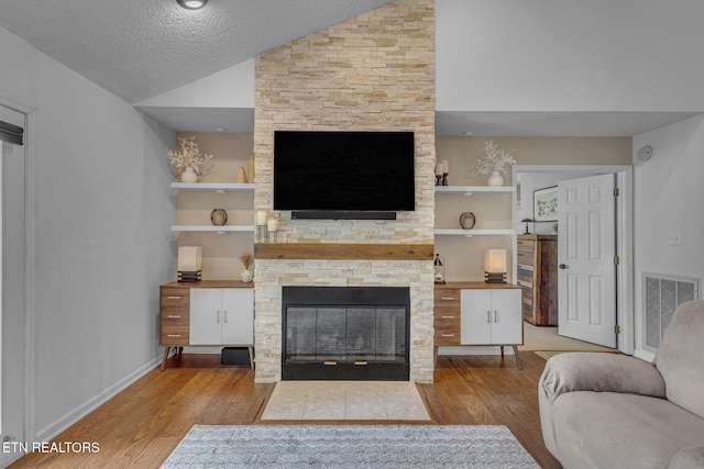 living room with wood finished floors, a stone fireplace, vaulted ceiling, built in features, and a textured ceiling