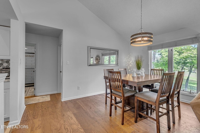 dining room with light wood-style floors, a chandelier, lofted ceiling, and baseboards