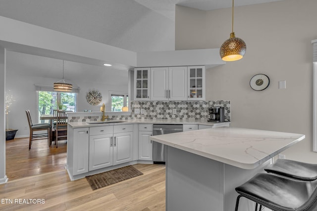 kitchen featuring a sink, stainless steel dishwasher, a peninsula, backsplash, and glass insert cabinets