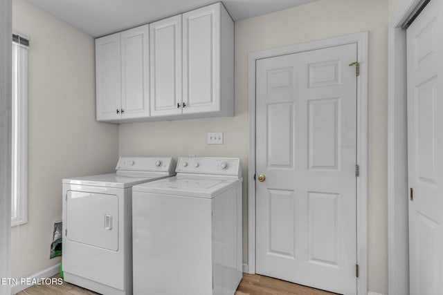 clothes washing area featuring separate washer and dryer, baseboards, cabinet space, and light wood-style floors