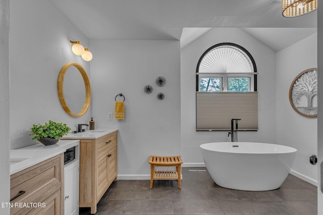 full bath with two vanities, baseboards, a freestanding tub, and lofted ceiling
