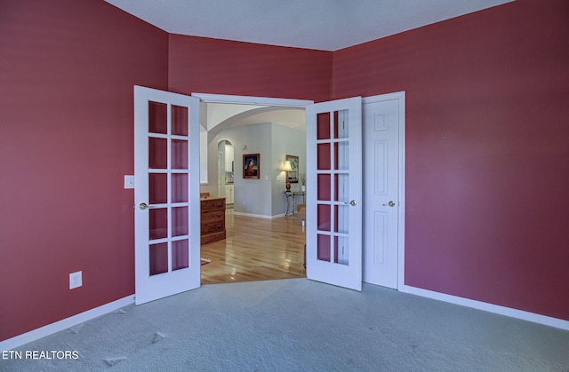 carpeted spare room with french doors, arched walkways, and baseboards
