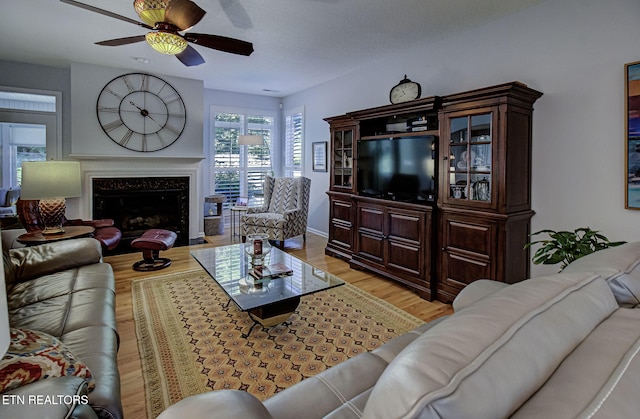 living area with light wood finished floors, a ceiling fan, and a premium fireplace