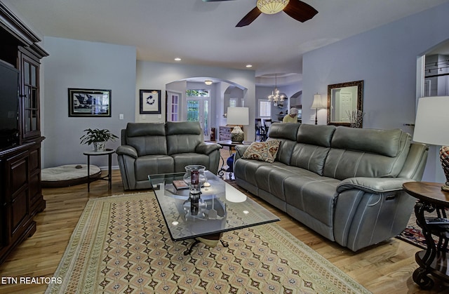 living room featuring arched walkways, a ceiling fan, light wood-style flooring, a chandelier, and recessed lighting