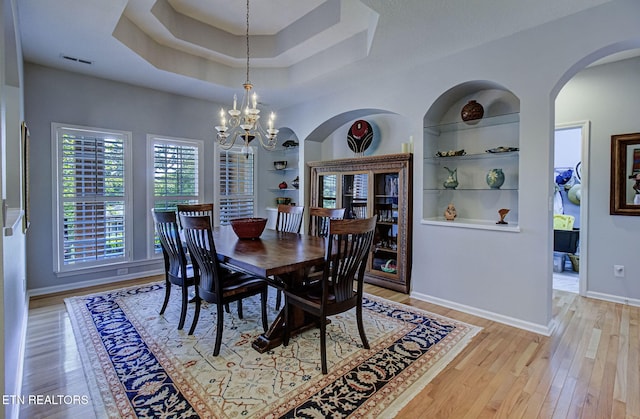 dining space with a chandelier, arched walkways, light wood-style floors, built in shelves, and baseboards