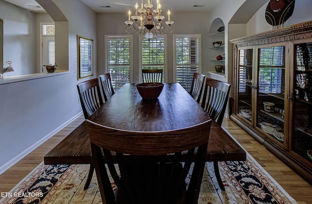 dining space featuring arched walkways, wood finished floors, built in features, baseboards, and a chandelier