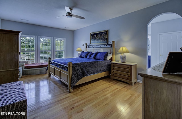 bedroom with arched walkways, light wood-type flooring, a ceiling fan, and baseboards
