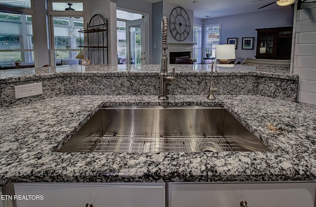 kitchen view of stone counters, a fireplace, ceiling fan, and a sink