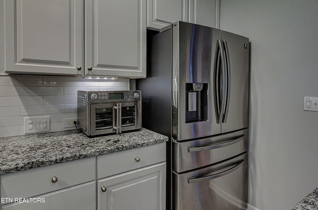 kitchen with stainless steel fridge with ice dispenser, backsplash, light stone counters, and white cabinets