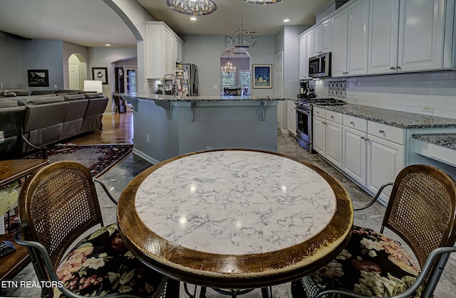 kitchen with stainless steel appliances, arched walkways, white cabinetry, stone counters, and recessed lighting