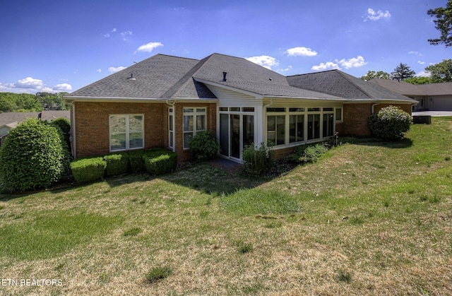 rear view of house with brick siding, a sunroom, a lawn, and roof with shingles