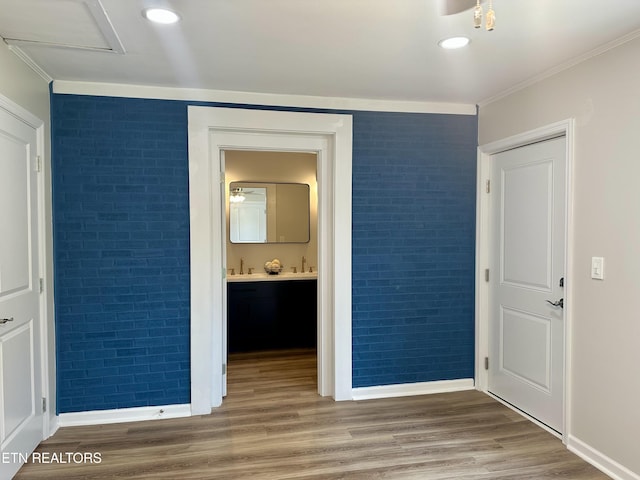 unfurnished bedroom with brick wall, baseboards, wood finished floors, crown molding, and ensuite bath