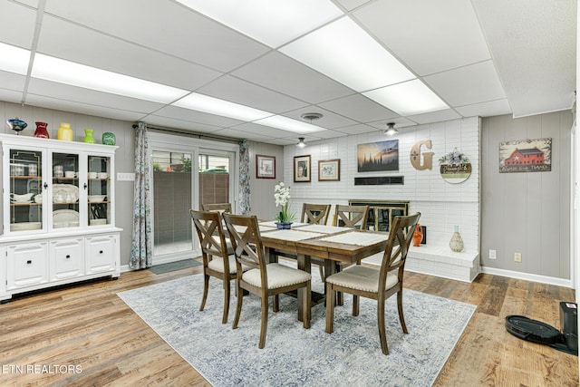 8000 Berkshire Blvd, Powell, TN 37849 - dining room featuring light wood finished floors, a paneled ceiling, wooden walls, baseboards, and a brick fireplace