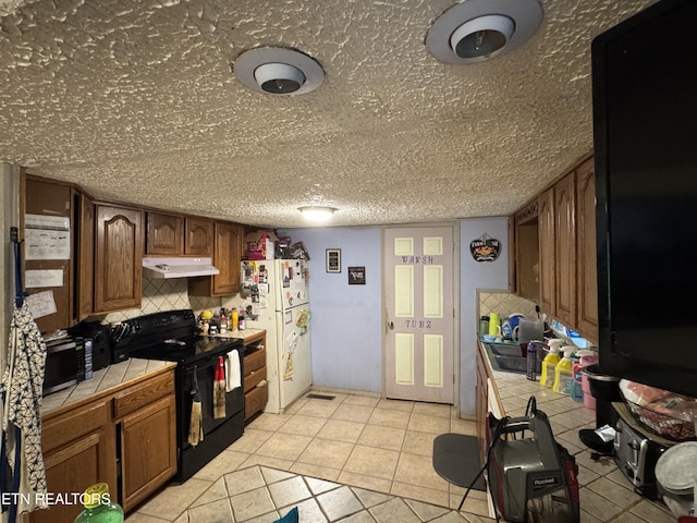 3441 Glendale Rd, Bybee, TN 37713 - kitchen featuring tile counters, black range with electric stovetop, freestanding refrigerator, under cabinet range hood, and light tile patterned floors