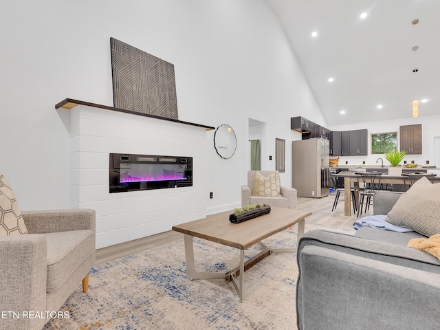 living area with light wood-style floors, a glass covered fireplace, recessed lighting, and high vaulted ceiling