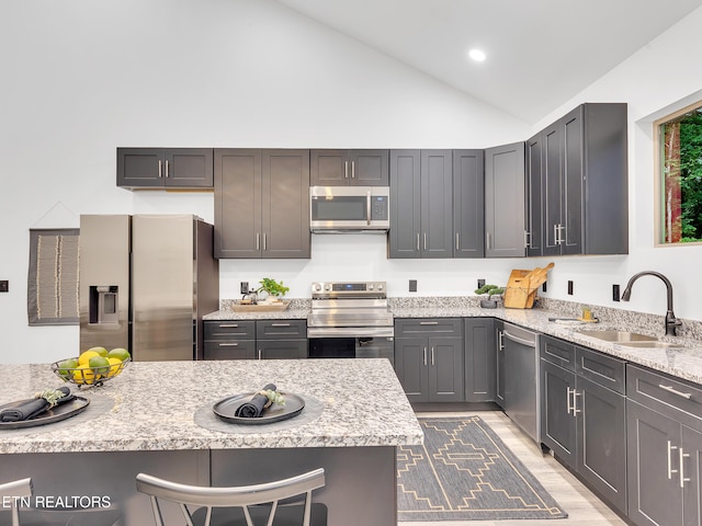 kitchen with stainless steel appliances, a sink, a breakfast bar, light stone countertops, and recessed lighting