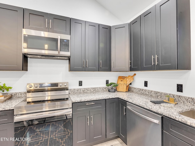 kitchen featuring stainless steel appliances, lofted ceiling, and light stone counters