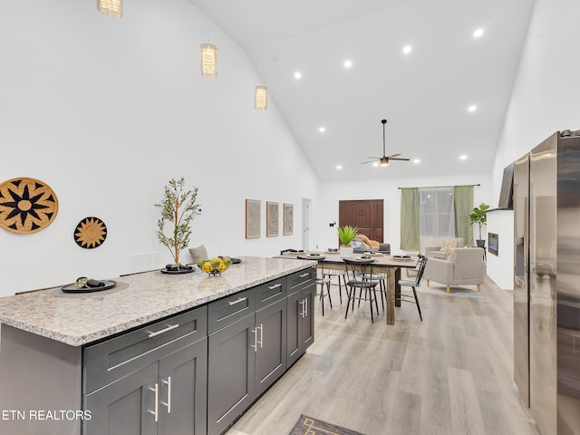 kitchen featuring stainless steel fridge, high vaulted ceiling, ceiling fan, a center island, and light wood-type flooring
