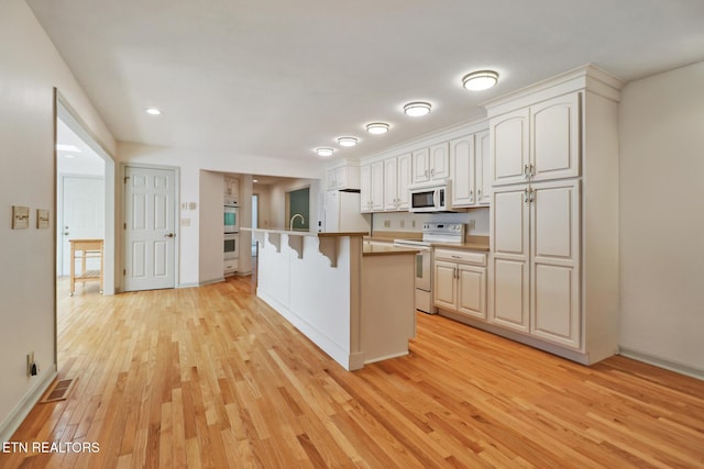 11 Kingsboro Ln, Crossville, TN 38558 - kitchen featuring white appliances, light wood-type flooring, a breakfast bar area, baseboards, and a center island with sink