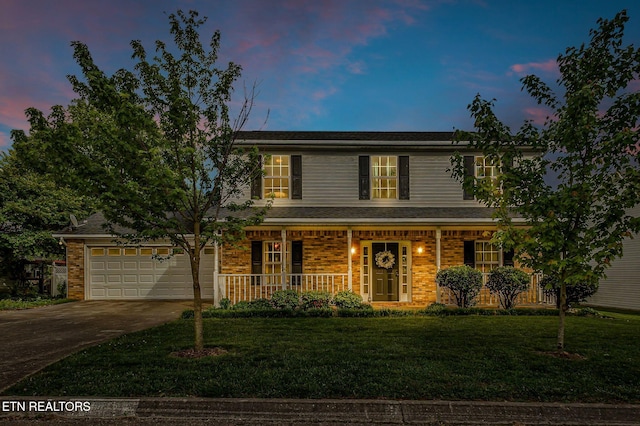 traditional home with covered porch, driveway, a yard, an attached garage, and brick siding