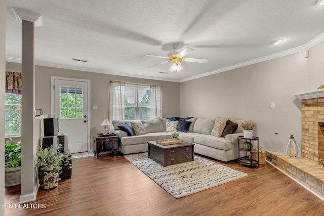 living area featuring a ceiling fan, wood finished floors, ornamental molding, a brick fireplace, and baseboards