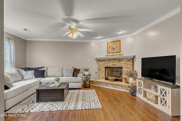 living room with wood finished floors, a ceiling fan, crown molding, a brick fireplace, and a textured ceiling